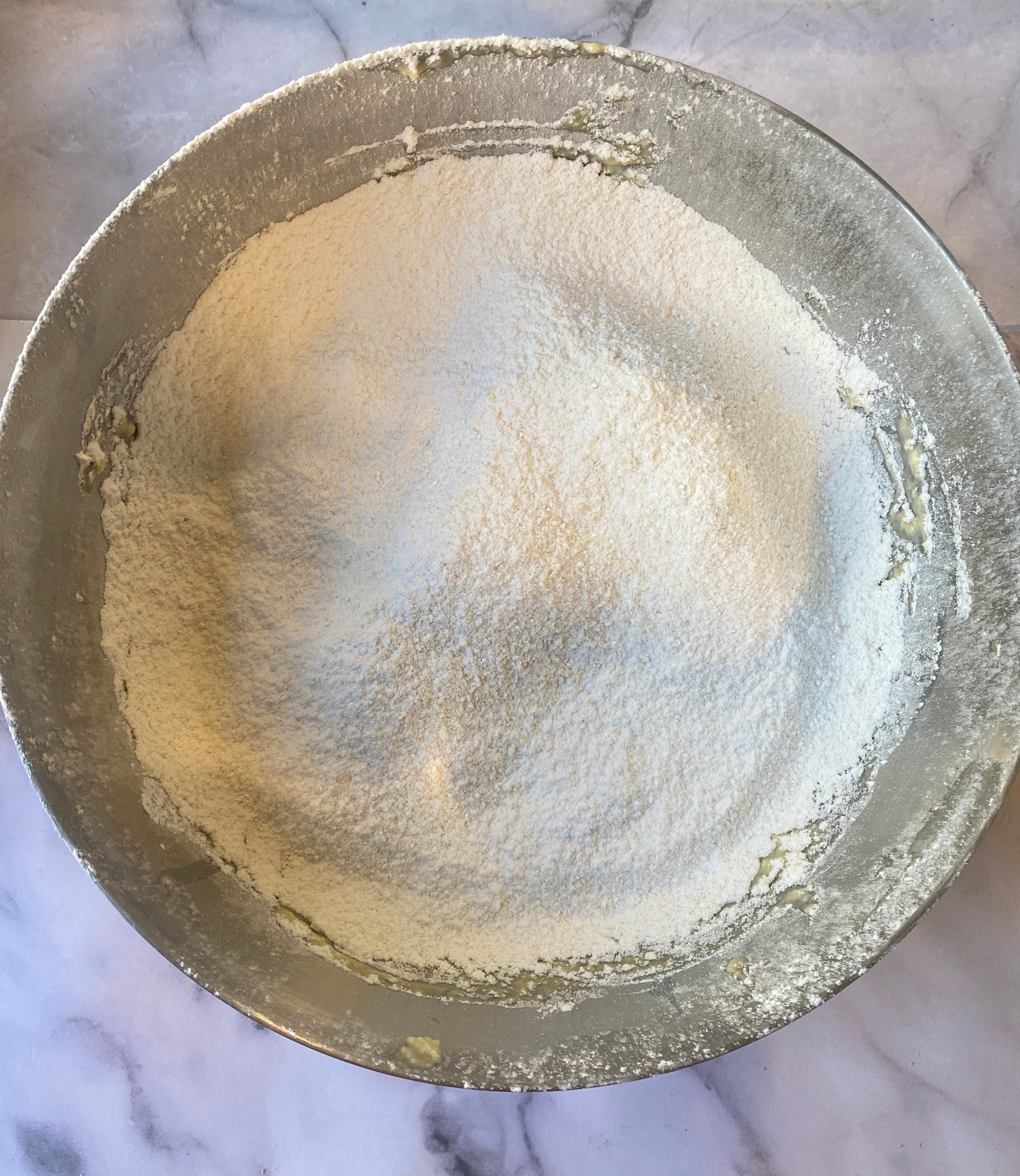 A mixing bowl filled with flour on a marble countertop, ready for baking