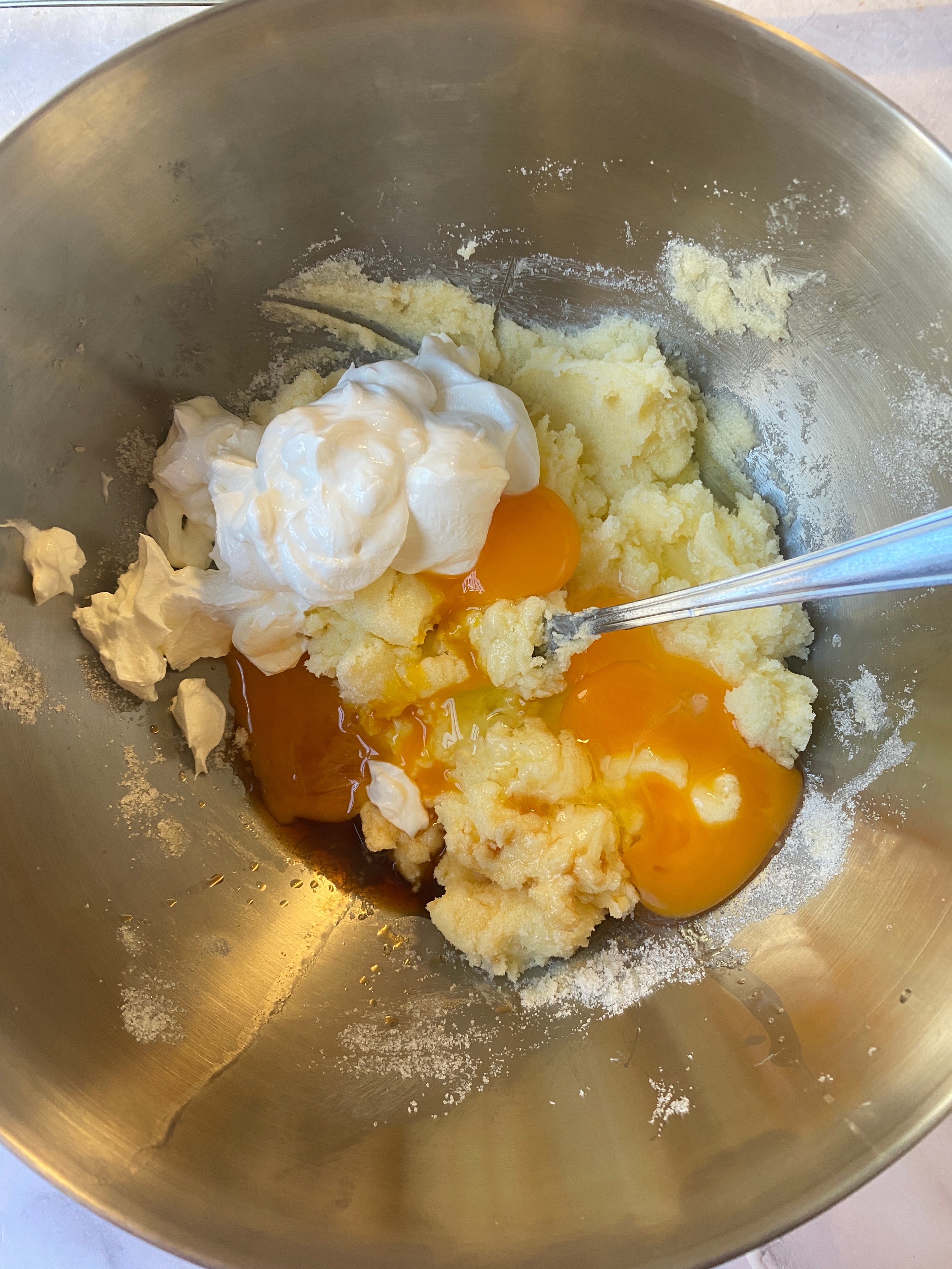 Bowl with butter, sugar, eggs, vanilla, and sour cream, partially mixed with a spoon, likely for baking