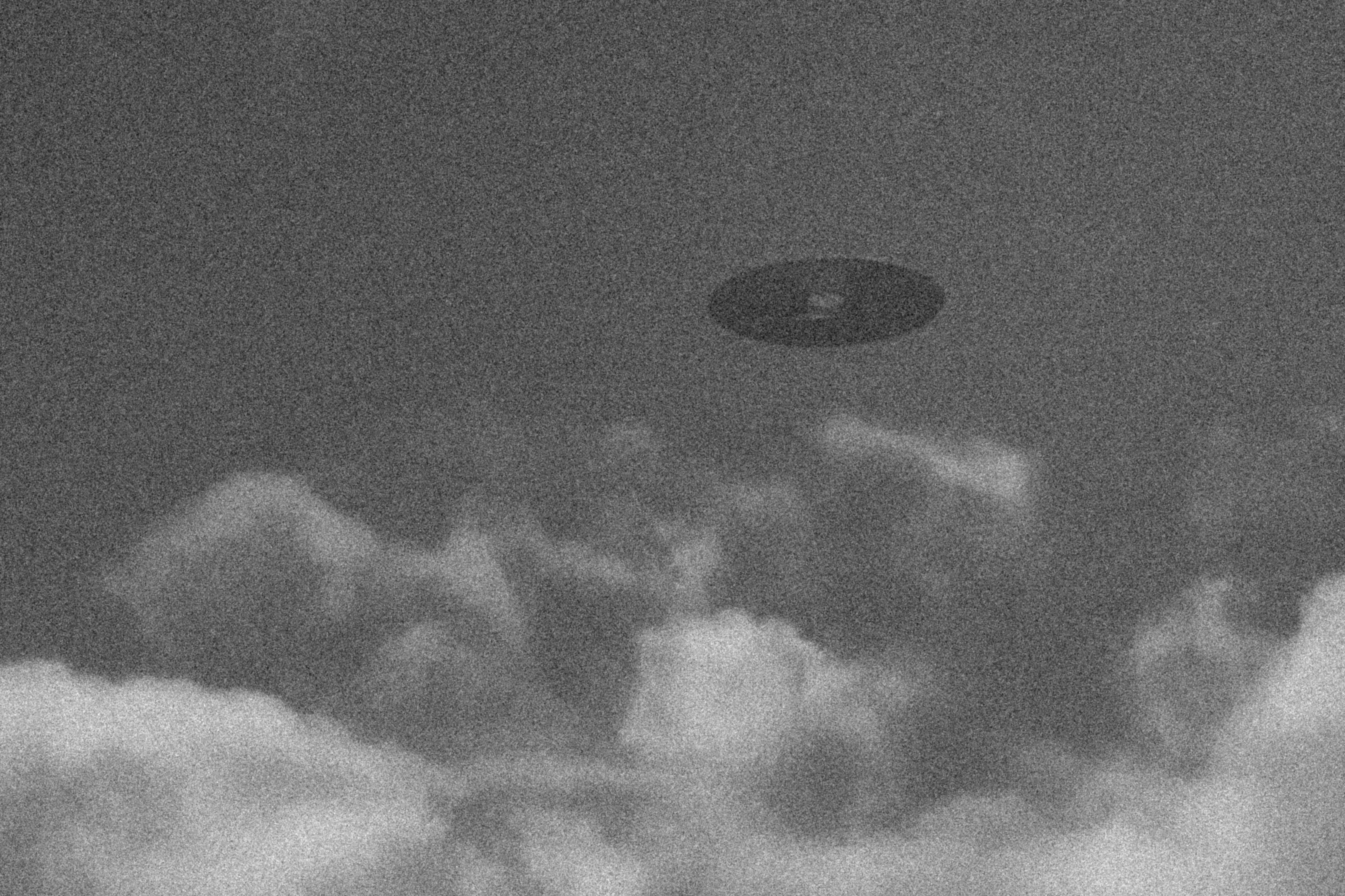 Kornet bilde av et skiveformet objekt på himmelen blant skyer, som ligner et klassisk UFO-observasjon