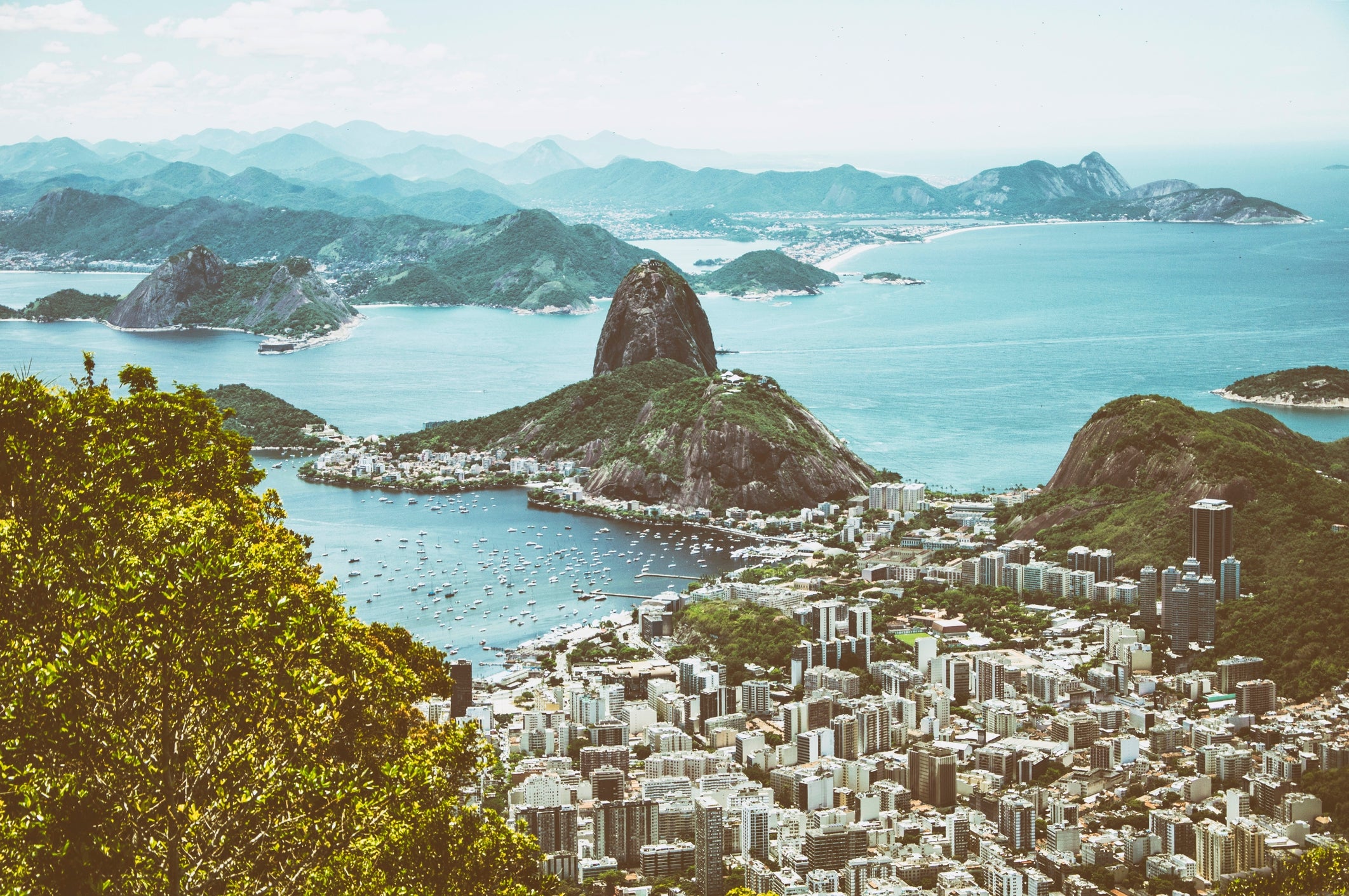 Luftfoto av Rio de Janeiro med Sukkertoppen, havet og bybildet rundt, innrammet av frodig grønt i forgrunnen