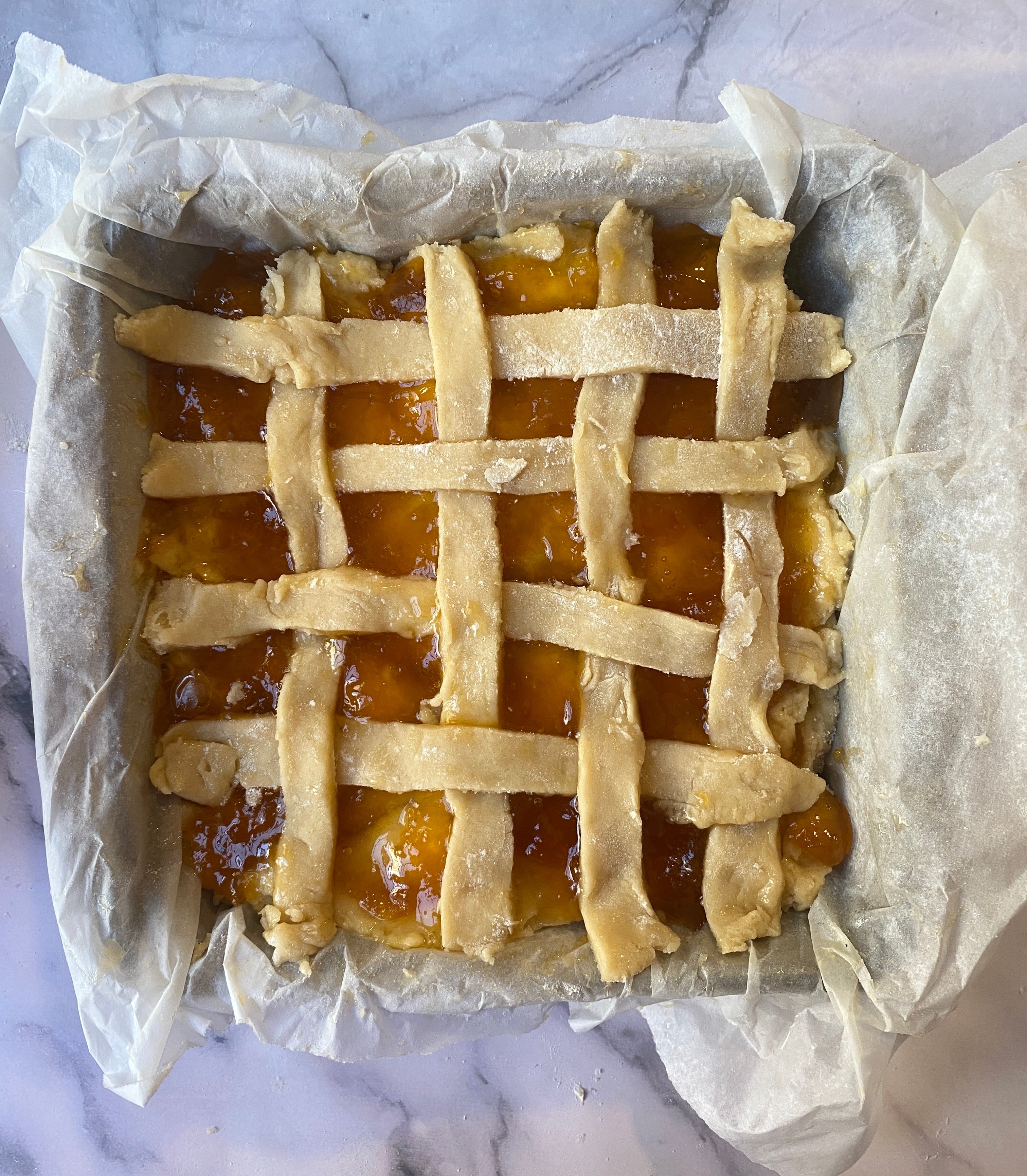 Lattice-top pie in a parchment-lined baking pan, resting on a marble surface