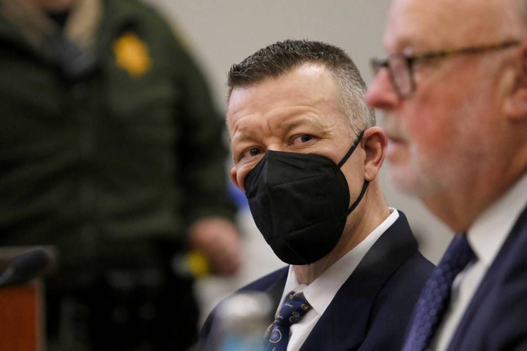 En mann i dress og slips iført svart maske ser intenst på en annen mann som snakker ved siden av ham