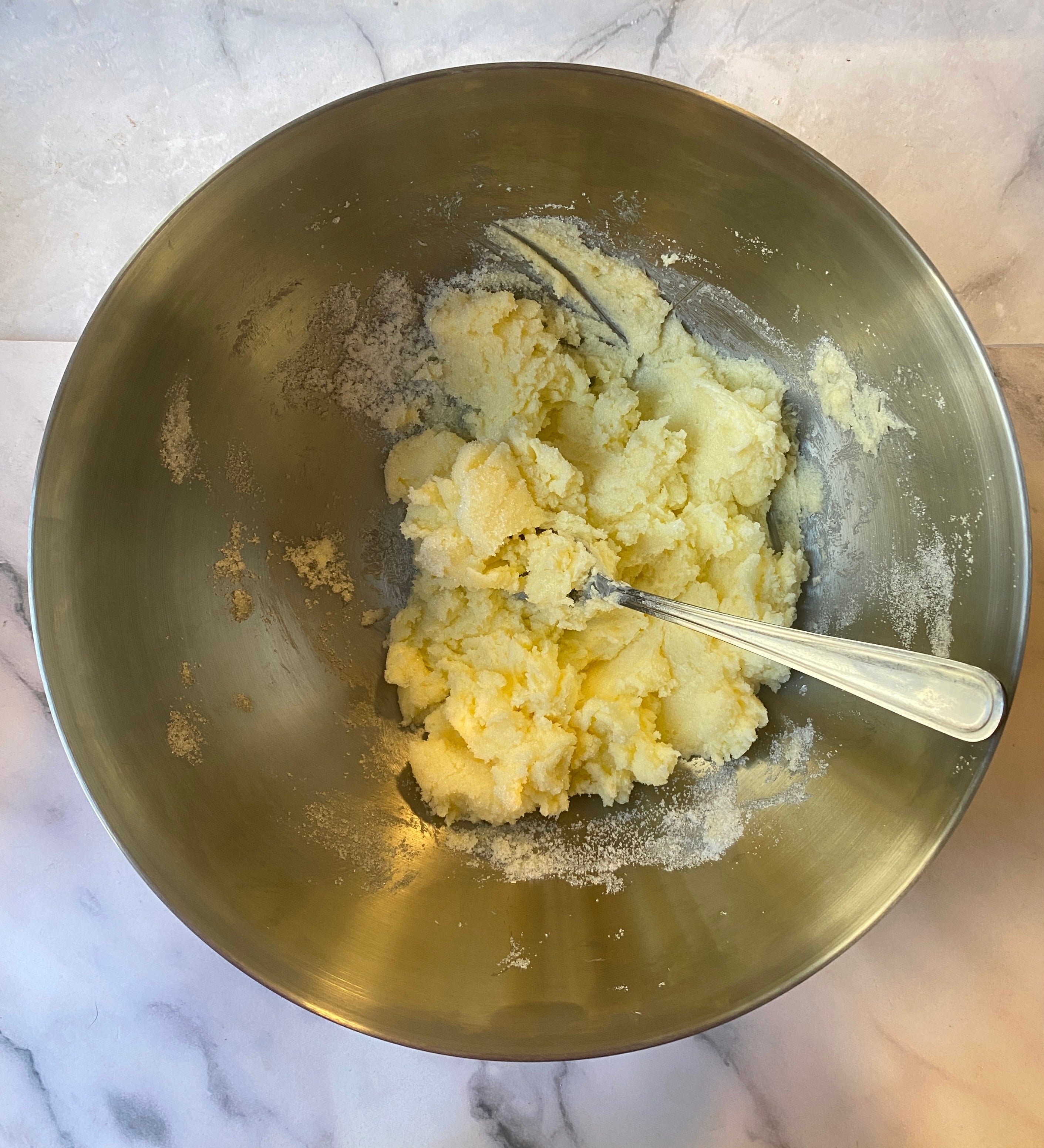 Butter and sugar creamed together in a mixing bowl with a metal spoon, likely for baking preparation