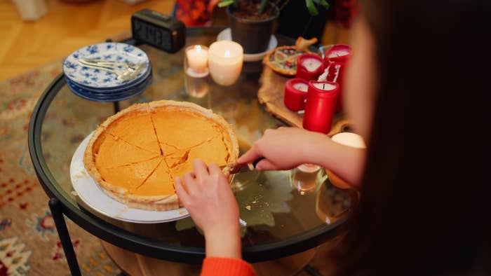 Person slicing a pumpkin pie on a round glass table with plates, candles, and decor