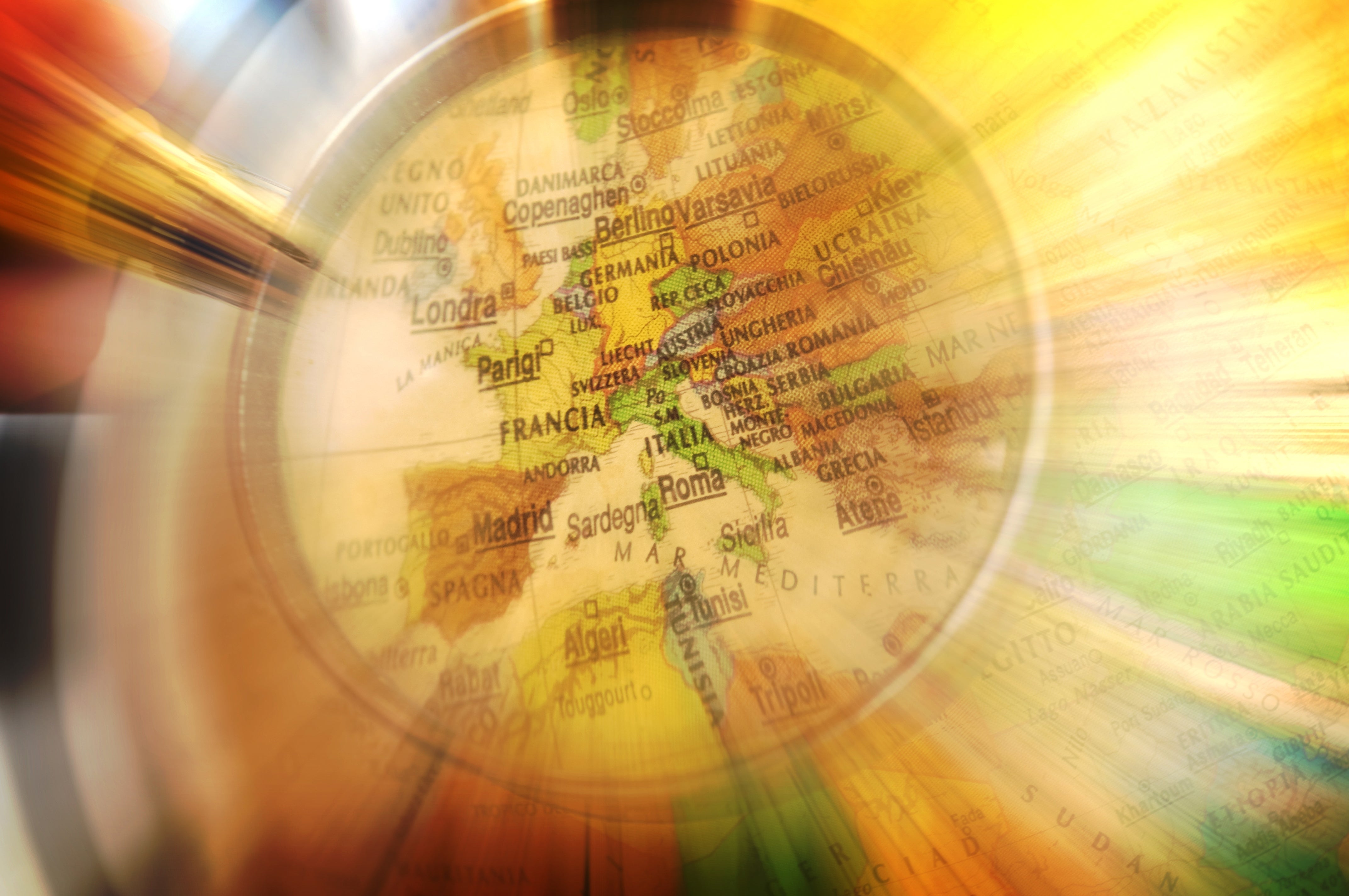 A close-up of a magnifying glass over a map of Europe, highlighting cities like Paris, Madrid, and Rome with a radiant effect around the edges