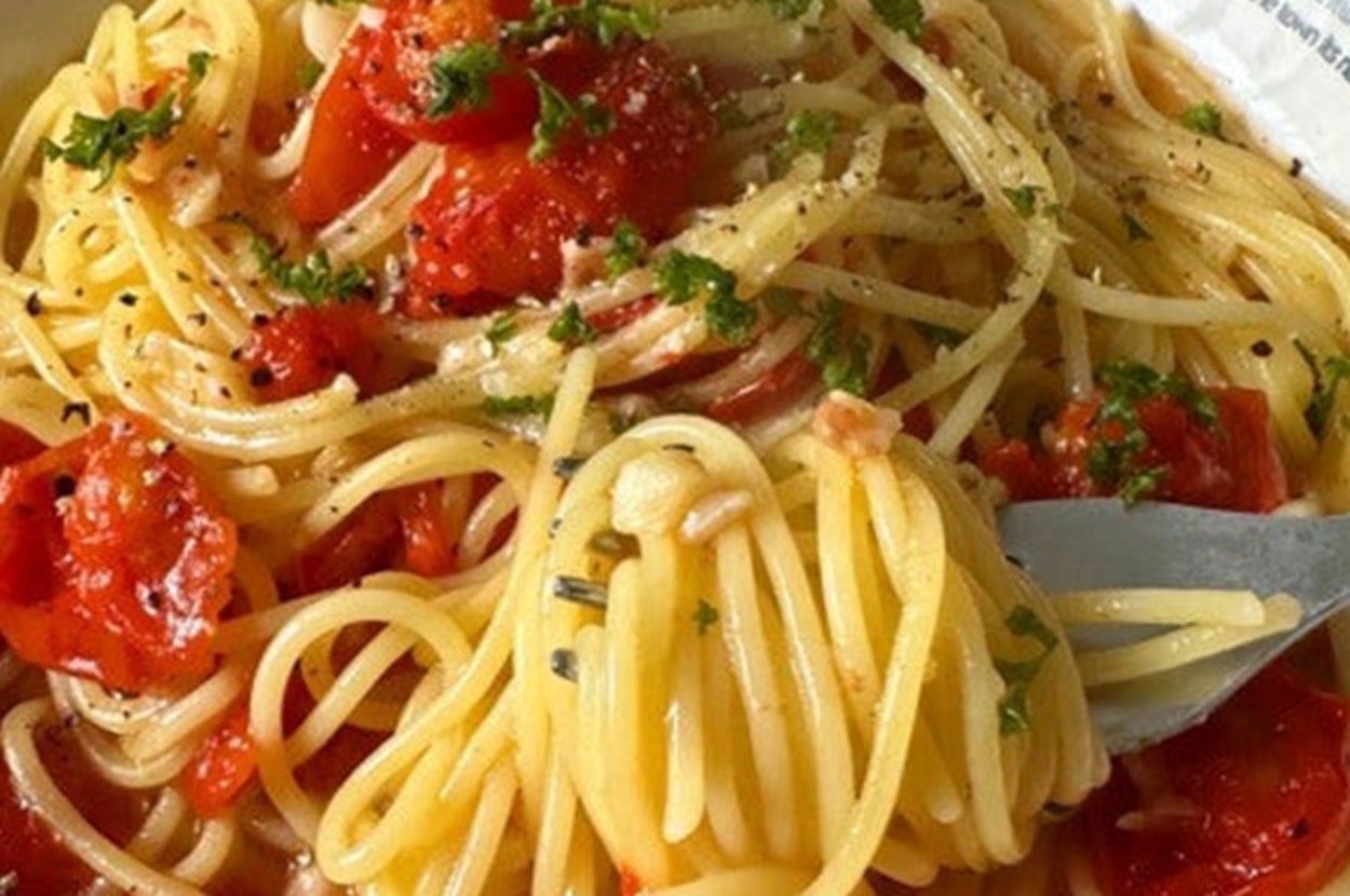 スパゲッティとトマト、ハーブが盛られたパスタ皿。背景に英字の装飾がある。