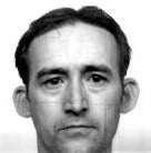 Man with short hair looking directly at the camera against a plain background