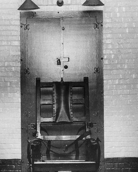 An old electric chair in an empty execution chamber, showcasing its straps and metal fittings