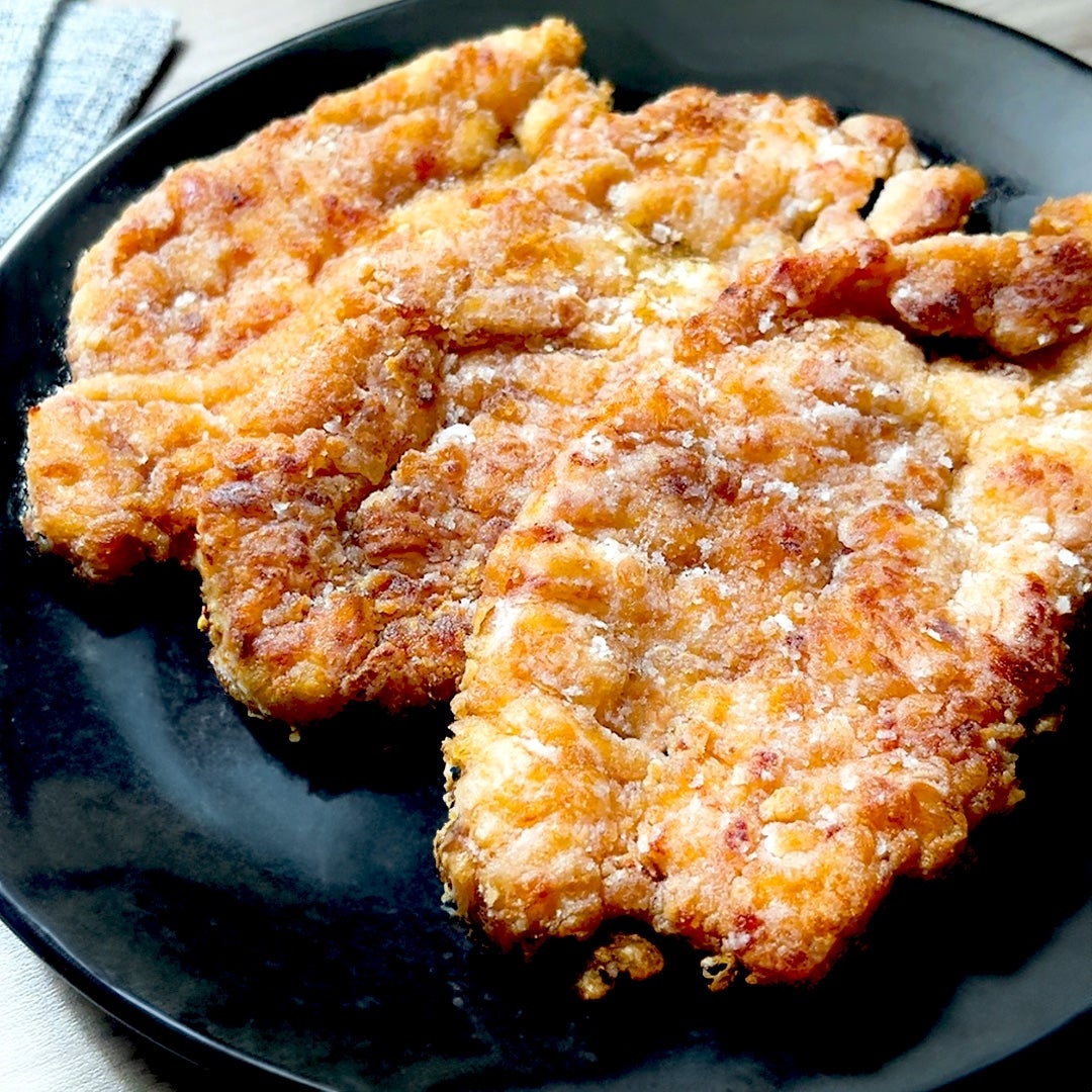 黒い皿に乗った揚げたチキンカツのクローズアップ。カリカリでジューシーな見た目。