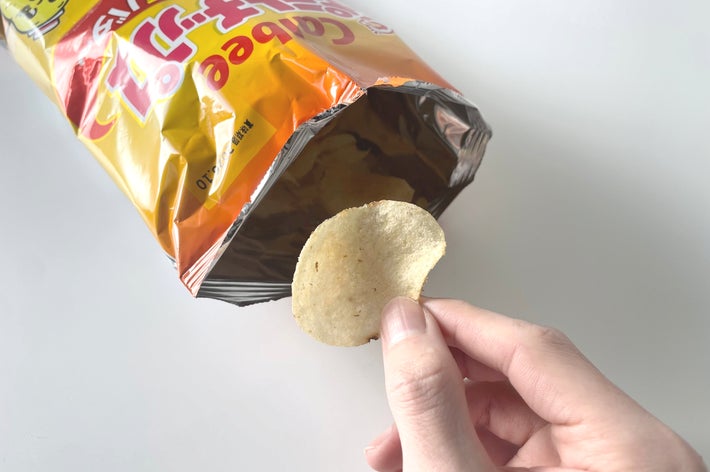開いたポテトチップスの袋からチップスを取り出す手。