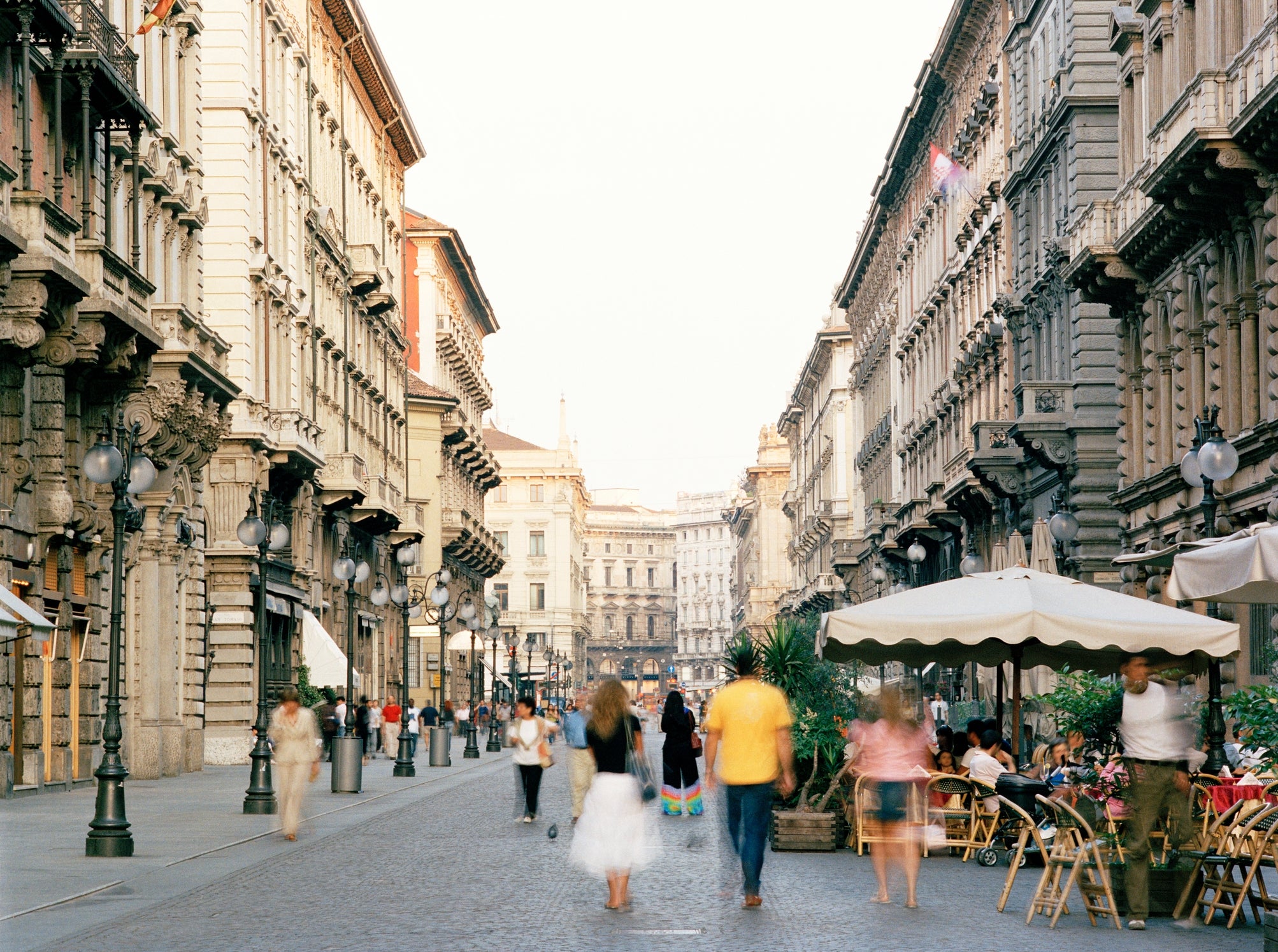 Bustling European street scene with historical architecture, outdoor cafe seating, and pedestrians strolling