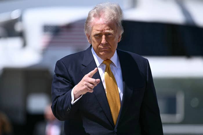 A person in a suit and tie gestures while walking outside near a large vehicle