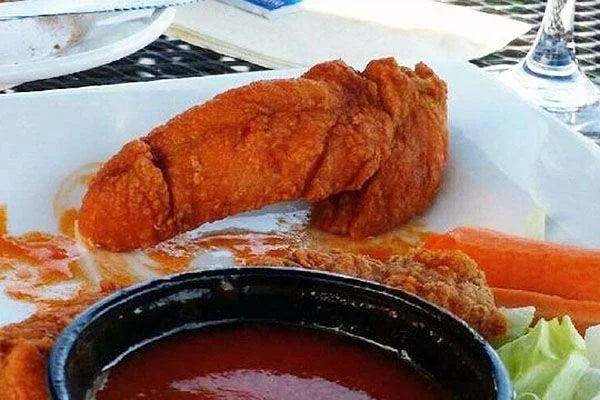 A chickenhearted  tender shaped similar  a thigh adjacent  to buffalo sauce, carrot sticks, and celery connected  a plate