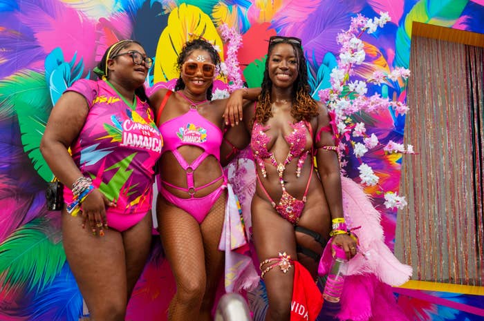 Three people in vibrant festival attire smiling in front of a colorful, feathered backdrop at a travel event