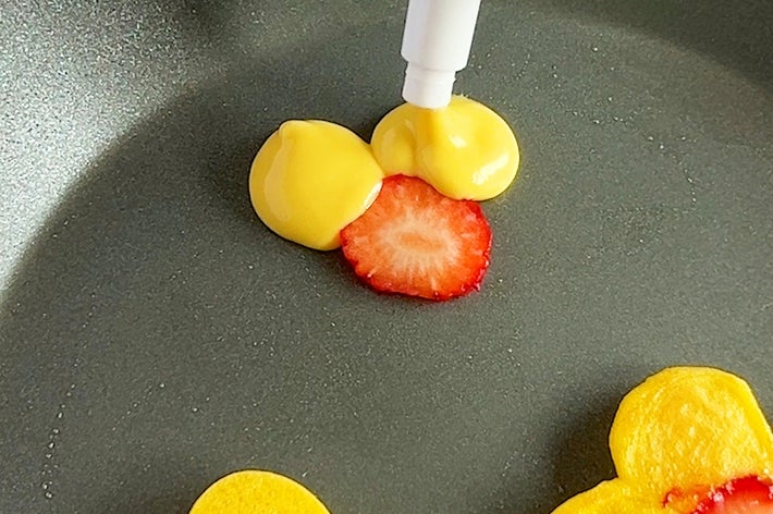 パンケーキ生地を花の形にフライパンで焼き、イチゴのスライスを中央に配置しています。