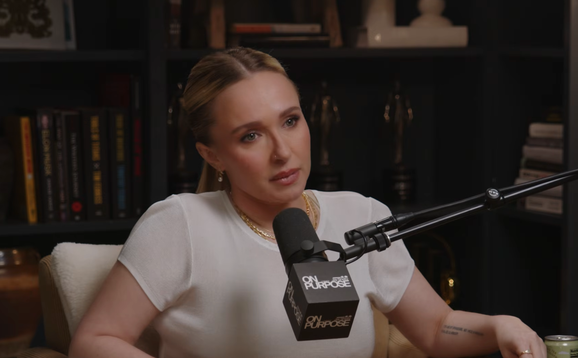 Person successful a podcast workplace wearing a simple, elegant outfit, speaking into a microphone labeled "On Purpose."