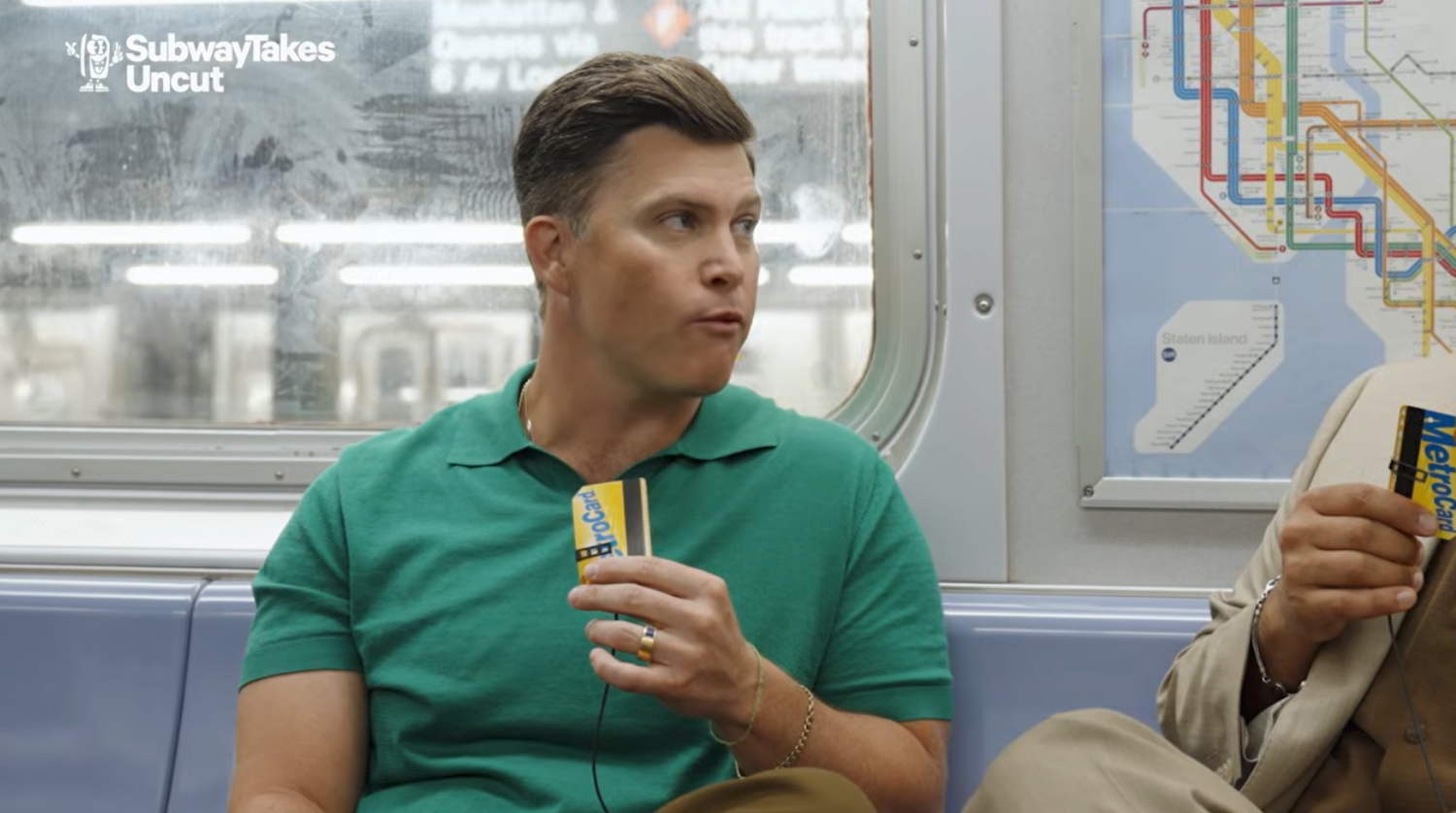 Person på T-banen som holder et MetroCard, iført en poloskjorte, snakker med noen utenfor kameraet. T-banekart synlig i bakgrunnen
