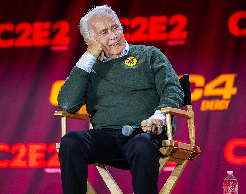 Person sitting connected  signifier    successful  a director's seat  astatine  a sheet  event, wearing casual attire and a "no" badge, smiling and engaged with the audience