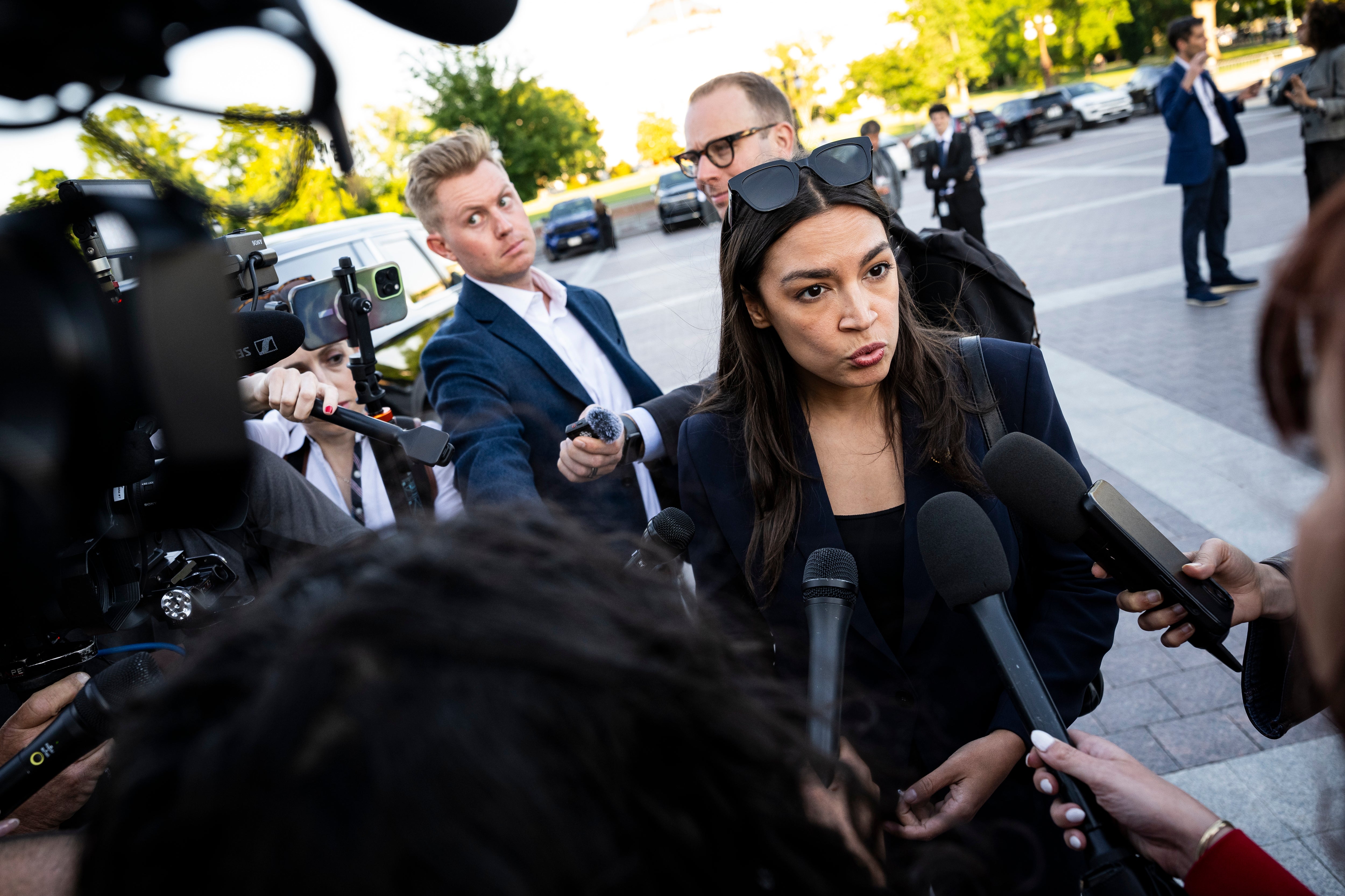 A pistillate successful concern attire addresses reporters with microphones outside, surrounded by cameras and media personnel