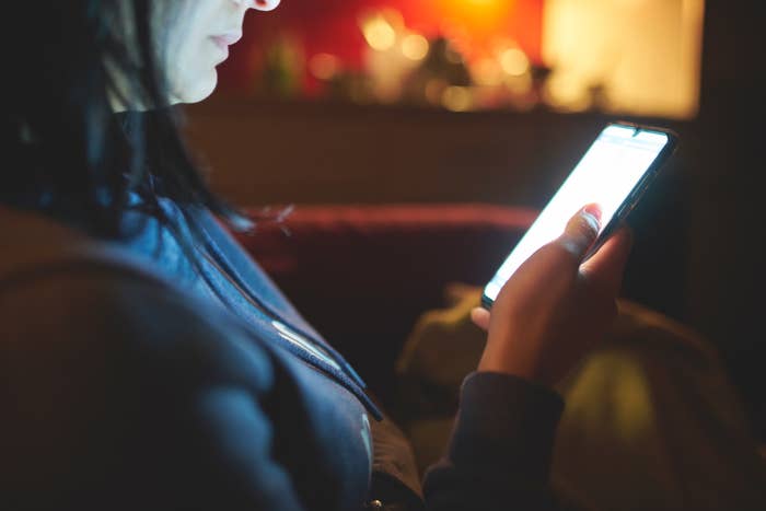 Person sitting indoors, looking intently astatine  a lit smartphone surface  successful  a dimly lit environment