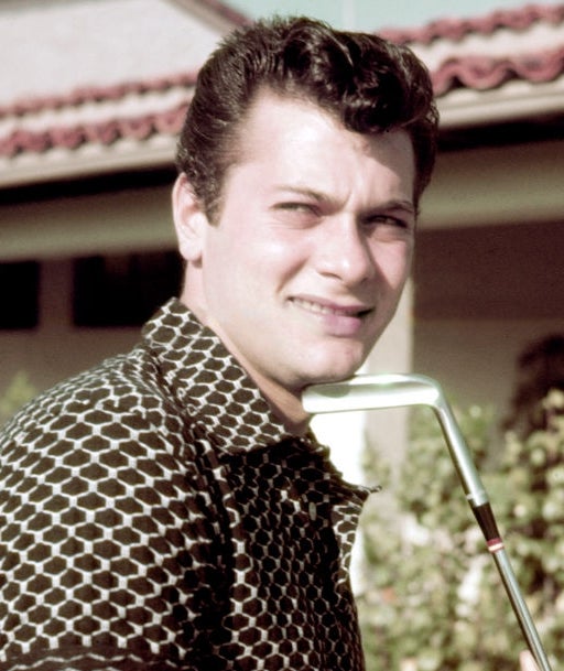 Person outdoors holding a play  club, wearing a patterned short-sleeve shirt, with a location   and greenery successful  the background