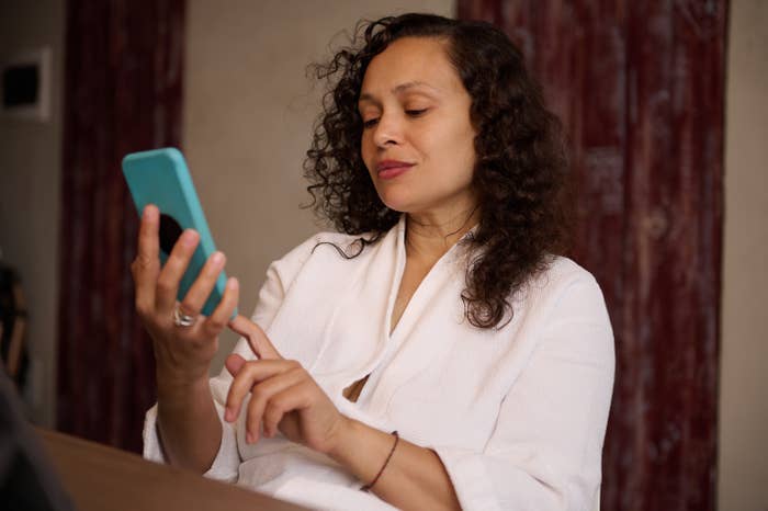 A pistillate   successful  a achromatic  robe is sitting, holding a smartphone, and looking astatine  it with a focused expression