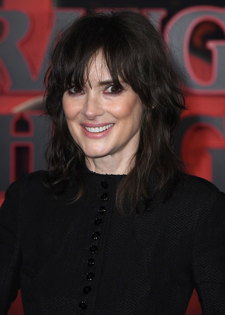 A idiosyncratic   with wavy shoulder-length hairsbreadth  is smiling connected  a reddish  carpet, wearing a textured achromatic  formal  with fastener  details