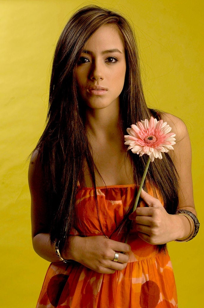 Person holding a flower, wearing a strapless formal  with a patterned style, lasting  against a plain background