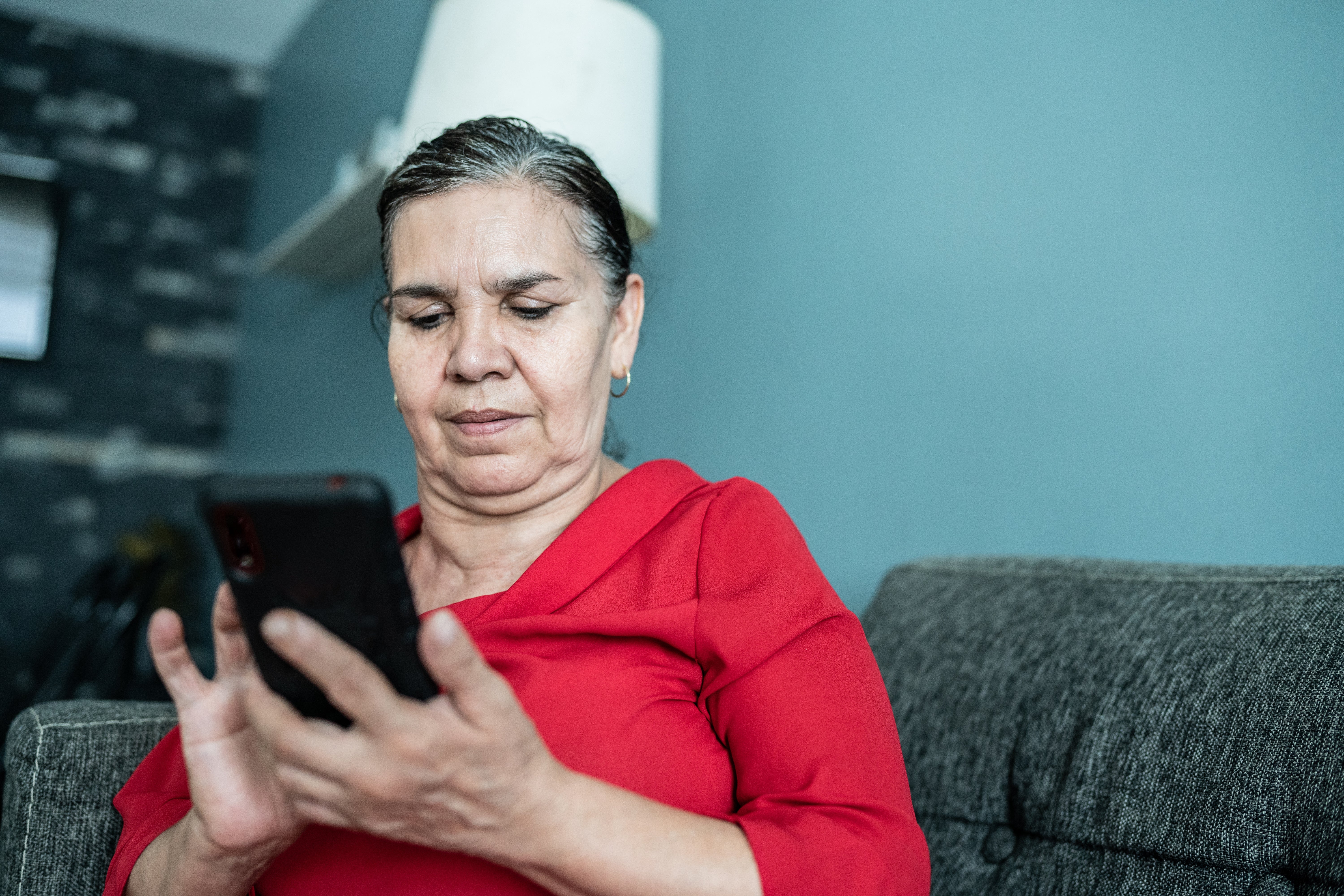 Older pistillate   seated connected  a couch, focused connected  utilizing a smartphone