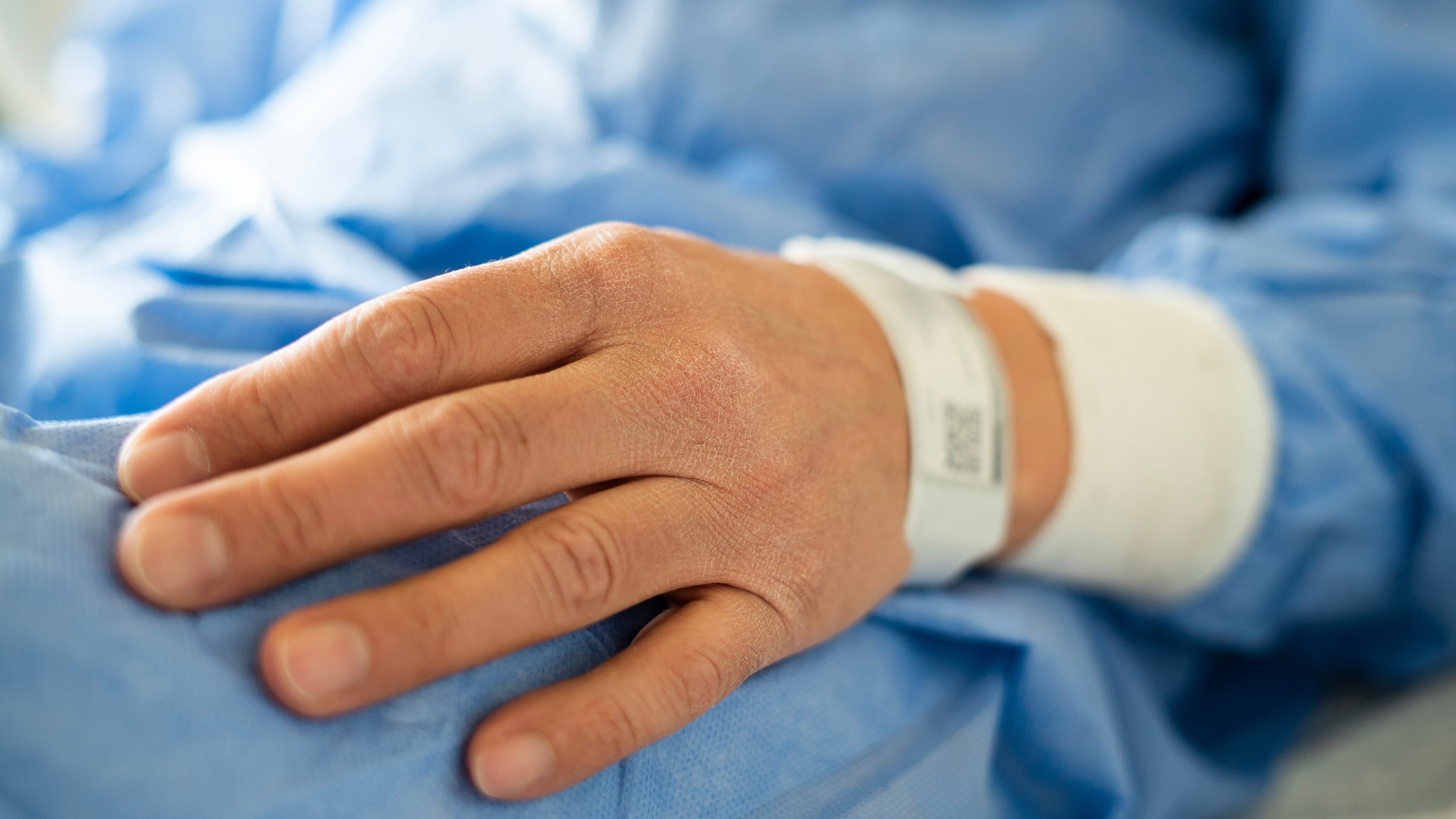 A close-up of a person's manus  with a infirmary  wristband resting connected  a bluish  cloth  surface