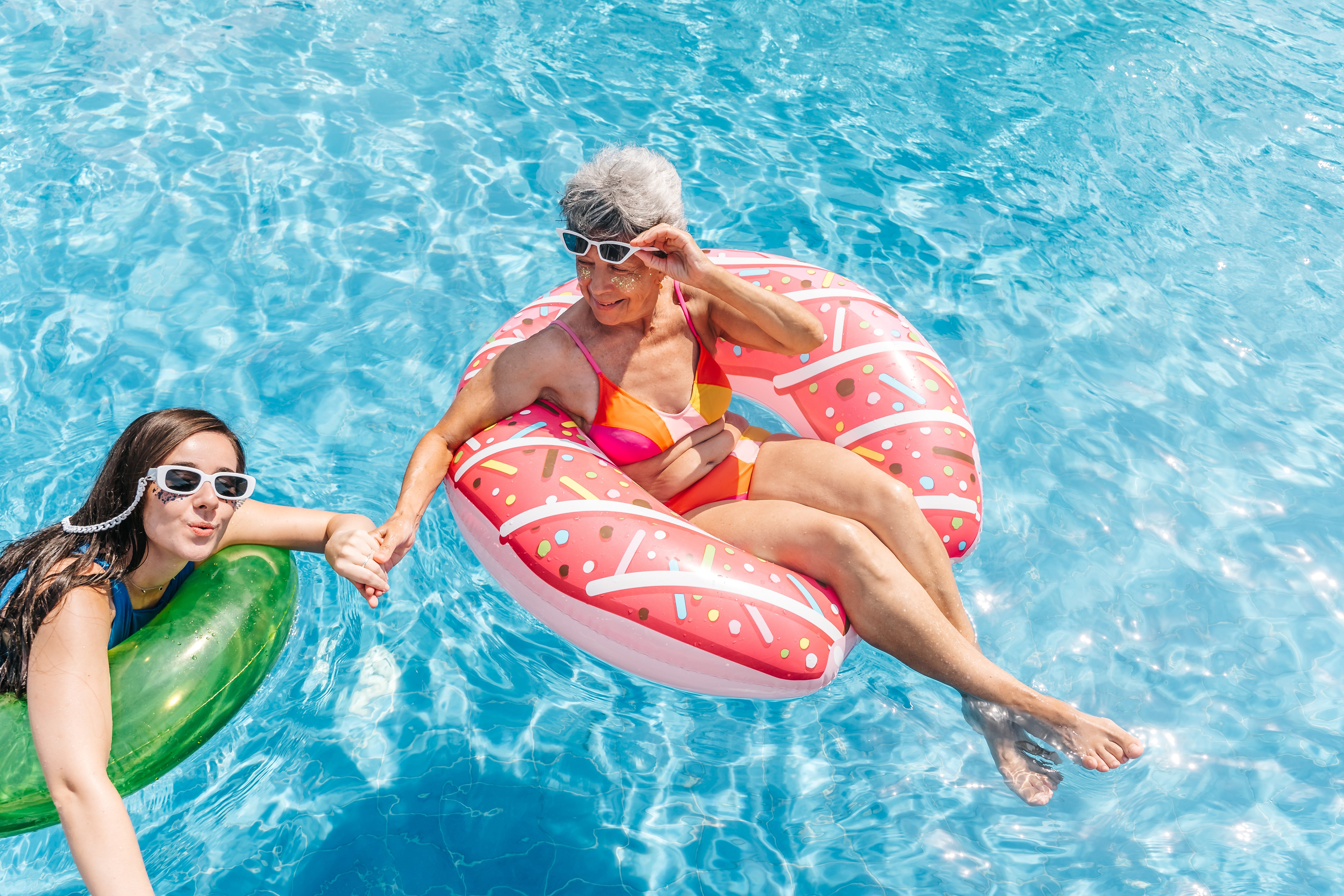 Two radical   with sunglasses bask  a pool; 1  successful  a donut interval  and the different   successful  a greenish  float, some  laughing and holding hands