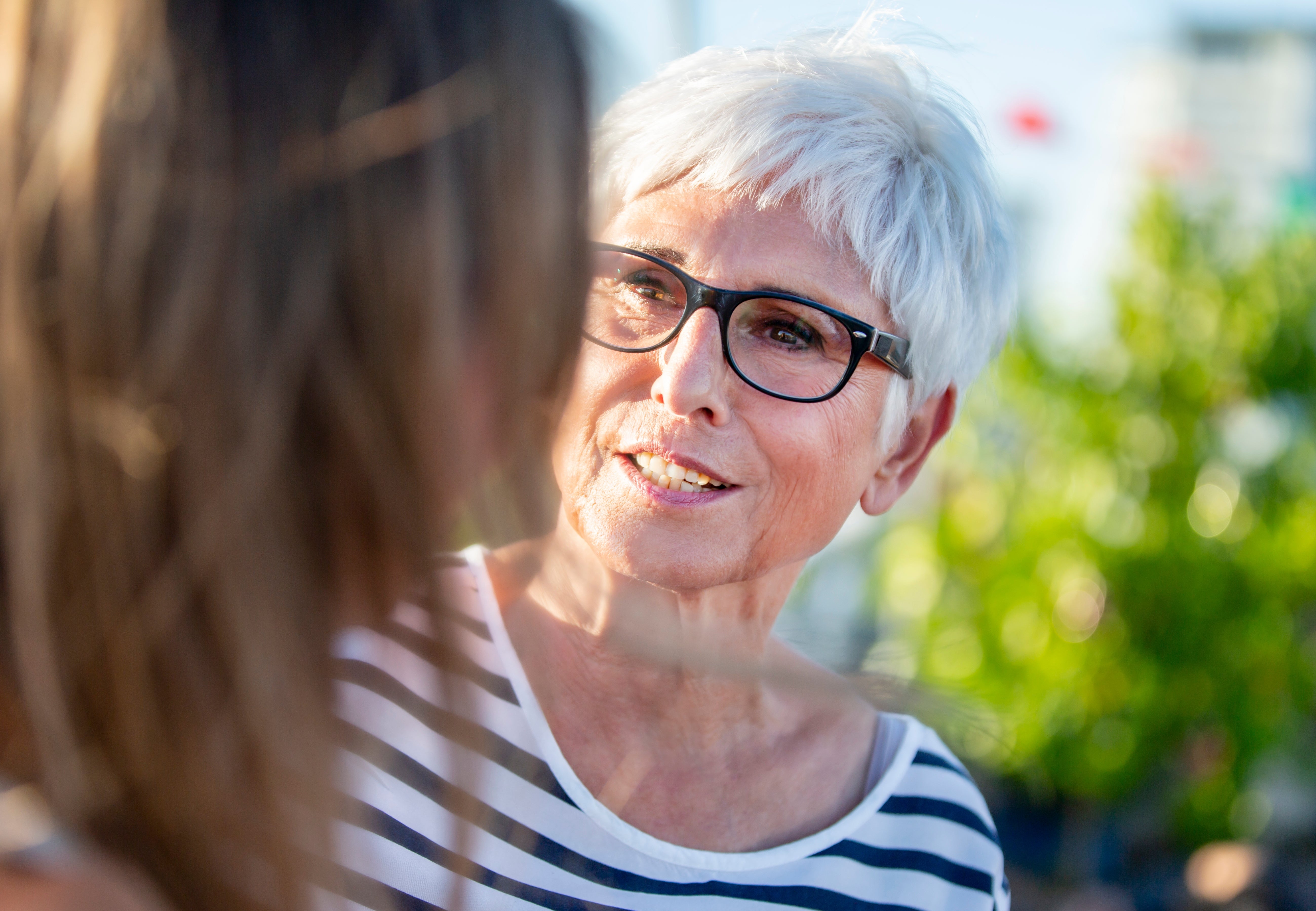 An older pistillate   with abbreviated  hairsbreadth  and glasses smiles portion    talking to different  idiosyncratic   outdoors