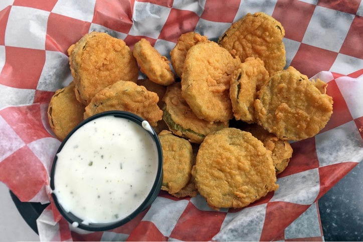 A basket of fried pickles with a side of dipping sauce on a checkered paper