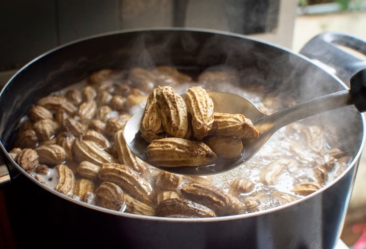 Boiling peanuts in a pot, with a ladle lifting some out. Steam rises from the water, suggesting they are freshly cooked
