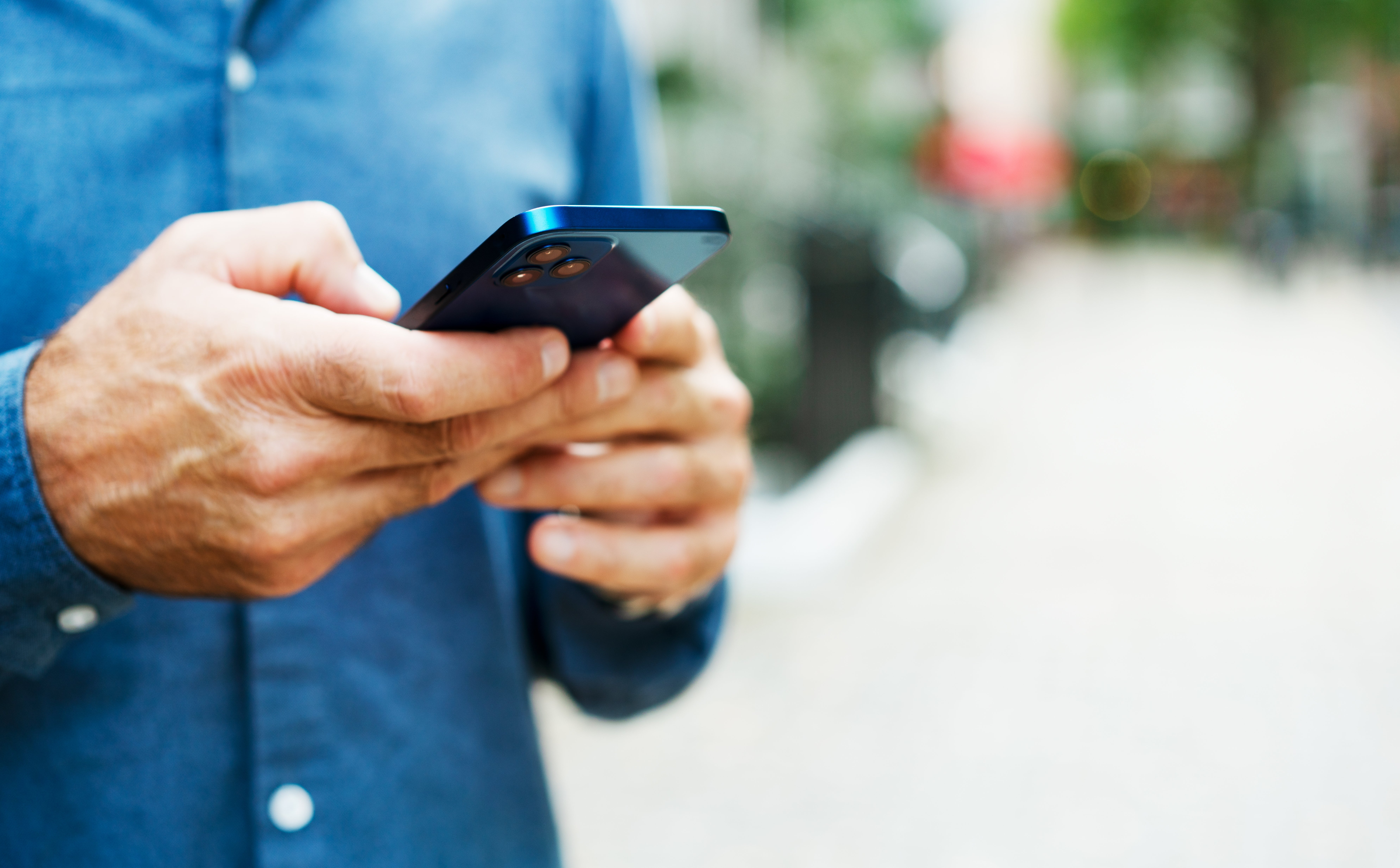 Person successful  denim garment  utilizing a smartphone outdoors. Focus connected  hands and device