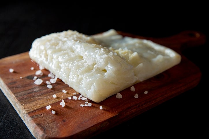 Salted cod on a wooden board, sprinkled with coarse salt