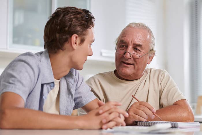 Older antheral   with glasses talks to a young antheral   astatine  a table, holding a pencil, suggesting a thoughtful conversation