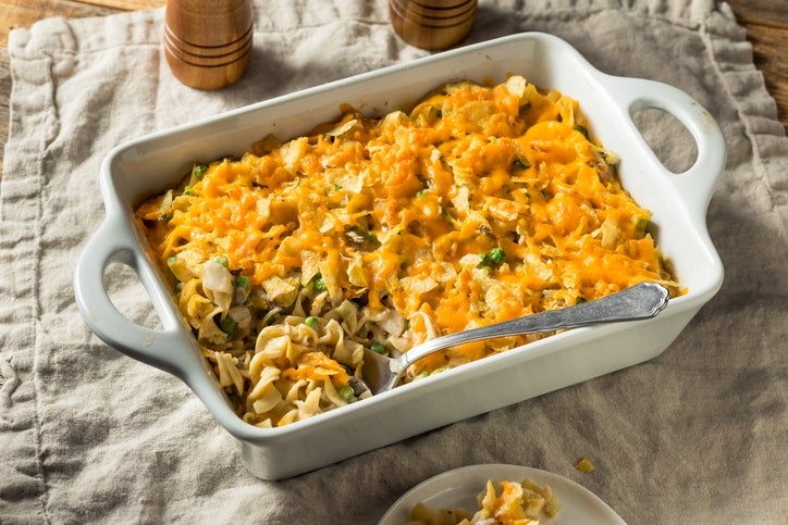 Baked casserole dish with noodles, shredded cheese, and vegetables on a textured cloth surface