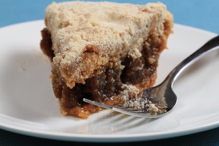 Slice of crumb-topped pie on a white plate with a fork, filled with a dark, sticky fruit filling