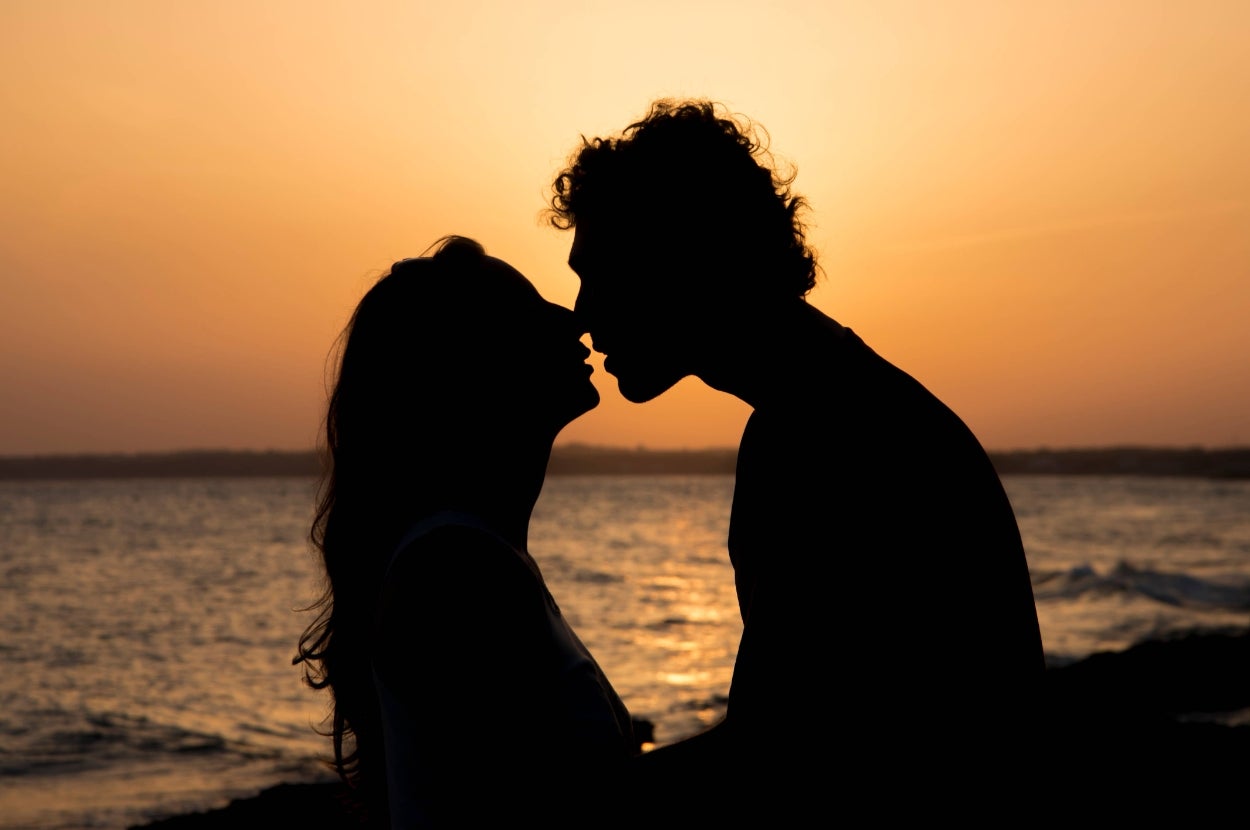 Silhouette of a couple about to kiss by the ocean at sunset, evoking romance and intimacy