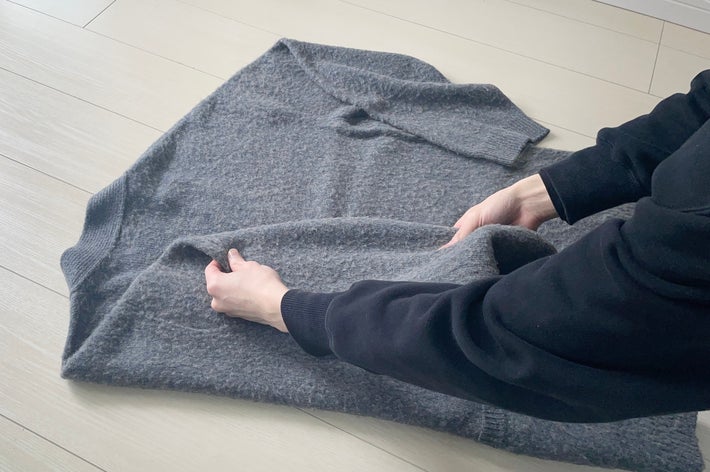 セーターを人が丁寧に畳んでいる様子。手元の動きに焦点。