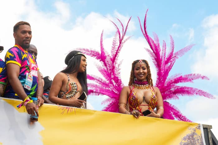 People in vibrant carnival costumes stand on a parade float, with colorful feathered accessories