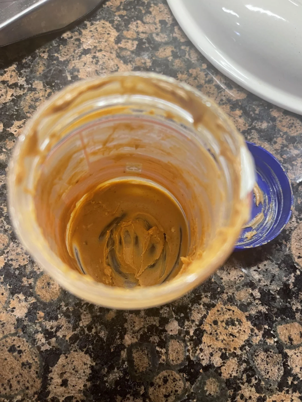 Empty peanut butter jar on a counter with remnants of peanut butter inside