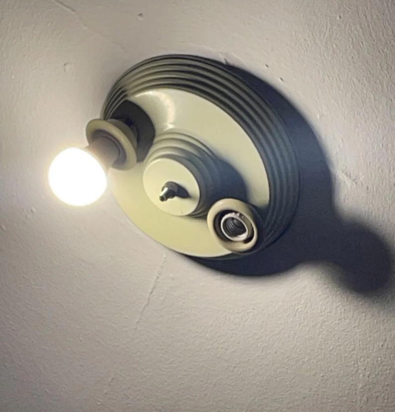 Ceiling-mounted light fixture with one lit bulb and two empty sockets casting shadows on the ceiling