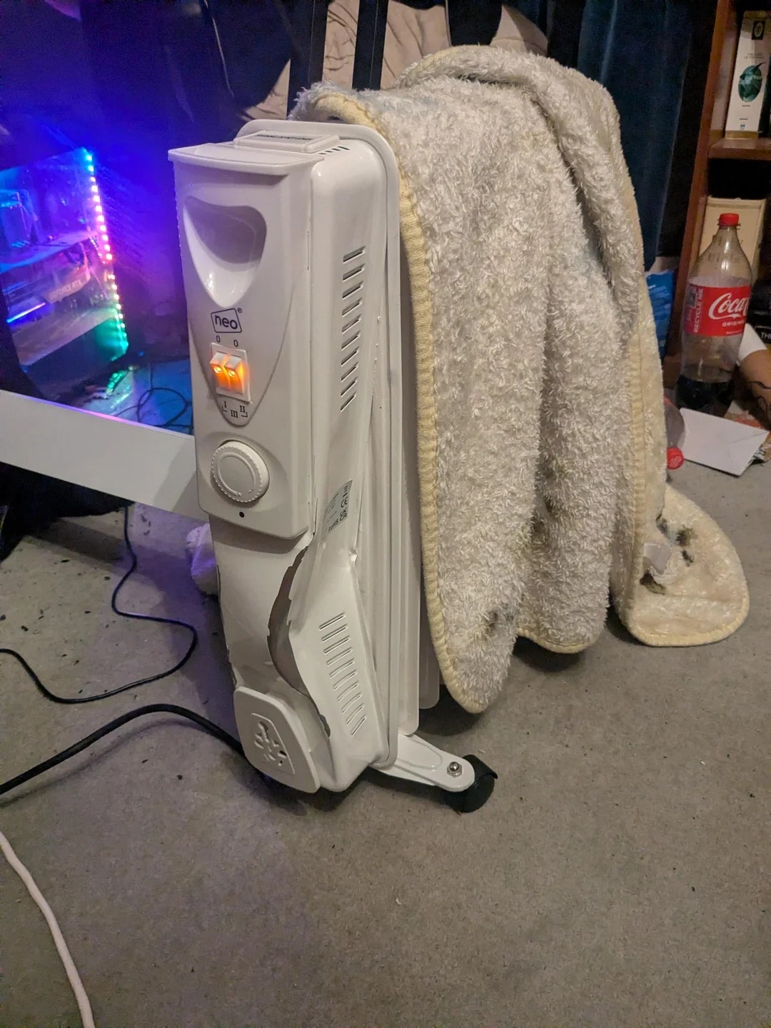 Heater with a blanket draped over it, in a cluttered room with a soda bottle on the floor