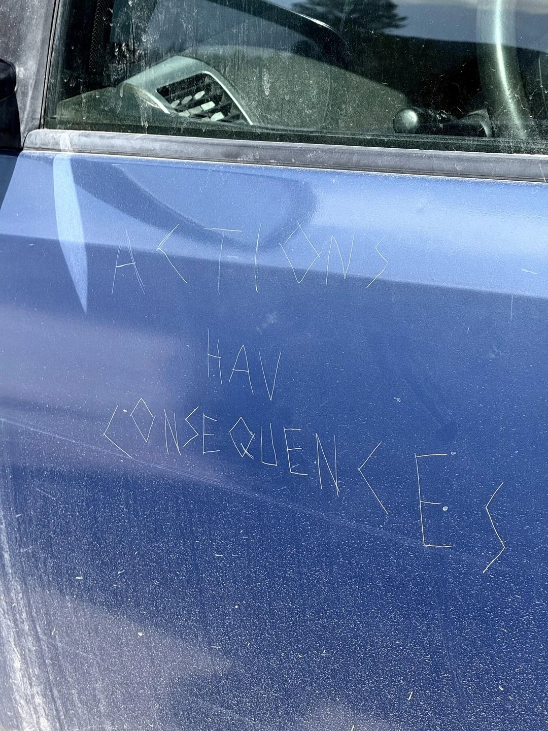 Scratched message on a car door reads, "ACTIONS HAVE CONSEQUENCES."