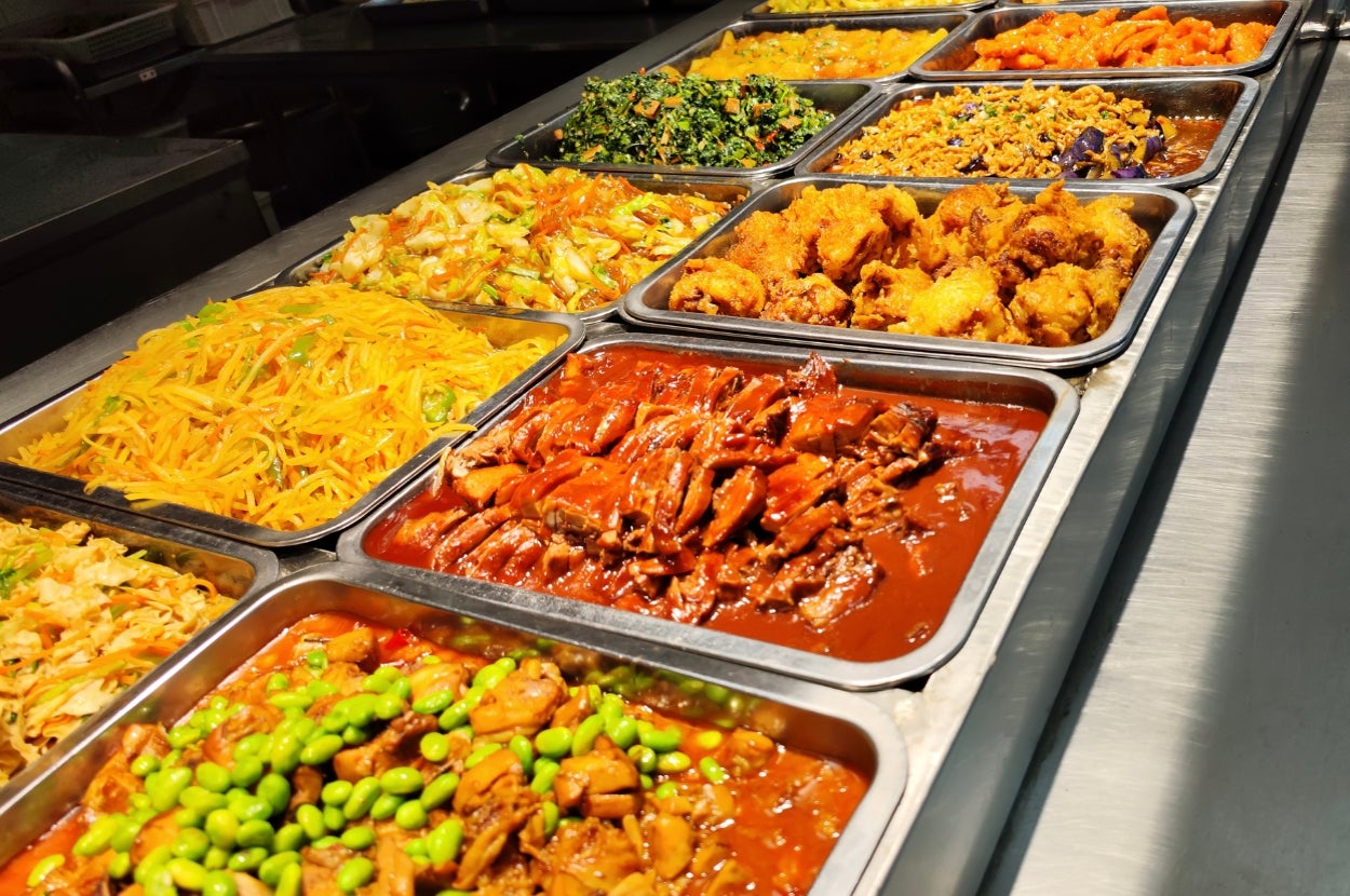 An array of assorted dishes in a buffet, including vegetables, meats, and fried items, displayed in metal trays