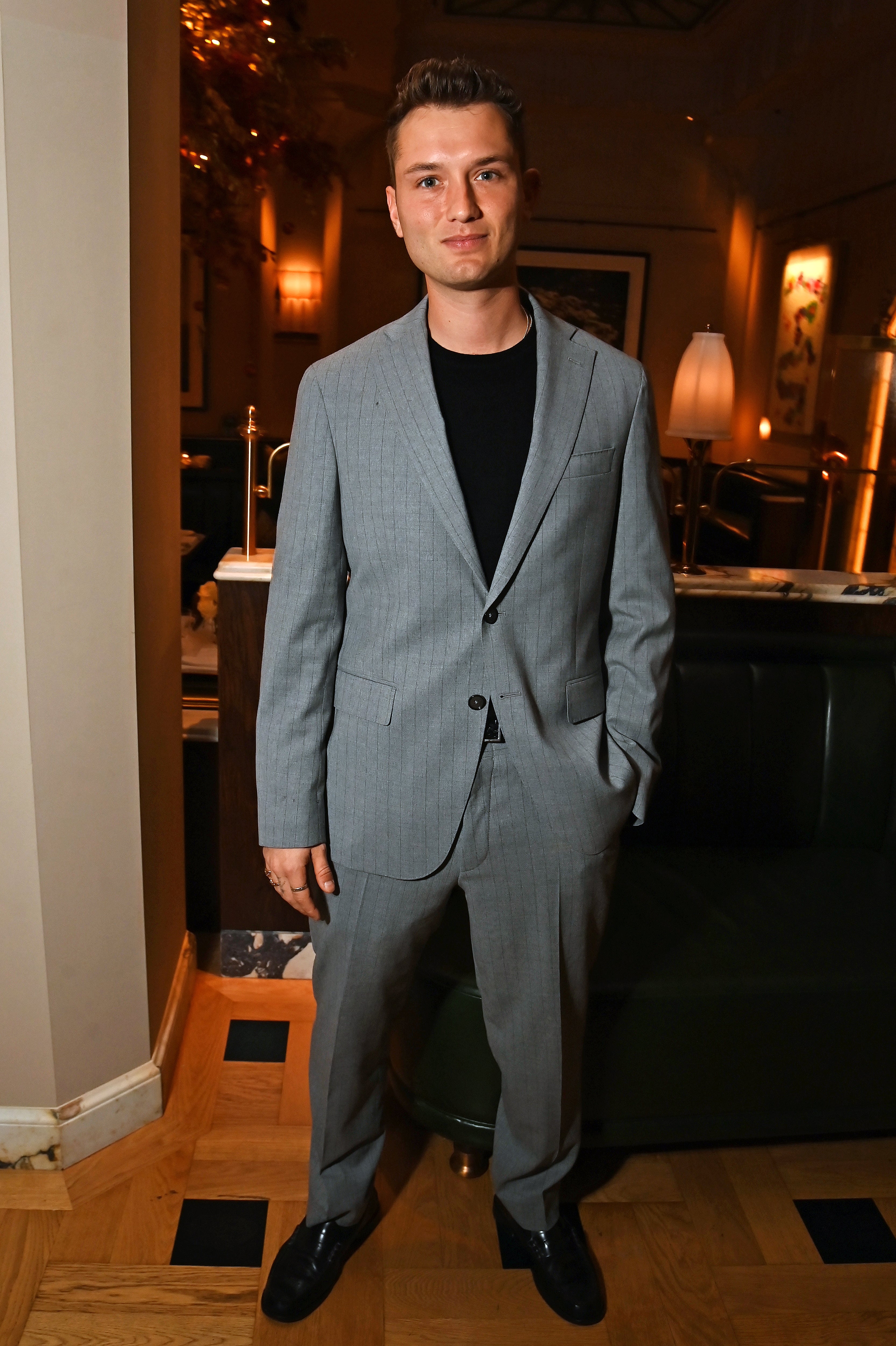 A idiosyncratic   successful  a stylish, tailored suit   and achromatic  garment  poses indoors astatine  an event, suggesting a blase  and ceremonial  occasion
