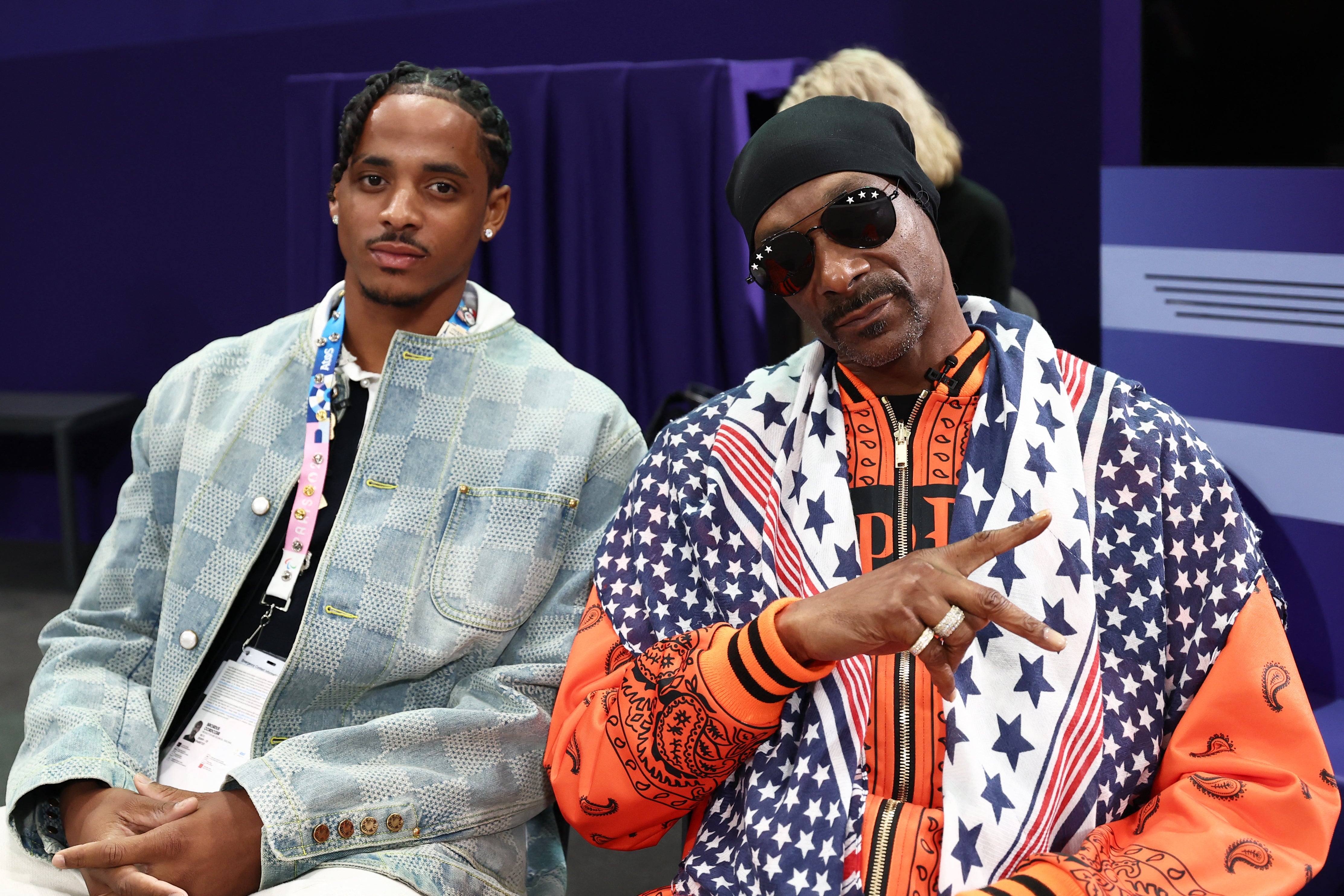 Two individuals are sitting, 1  successful  a denim jacket, and the different   successful  star-patterned attire and sunglasses, making a bid    motion   gesture