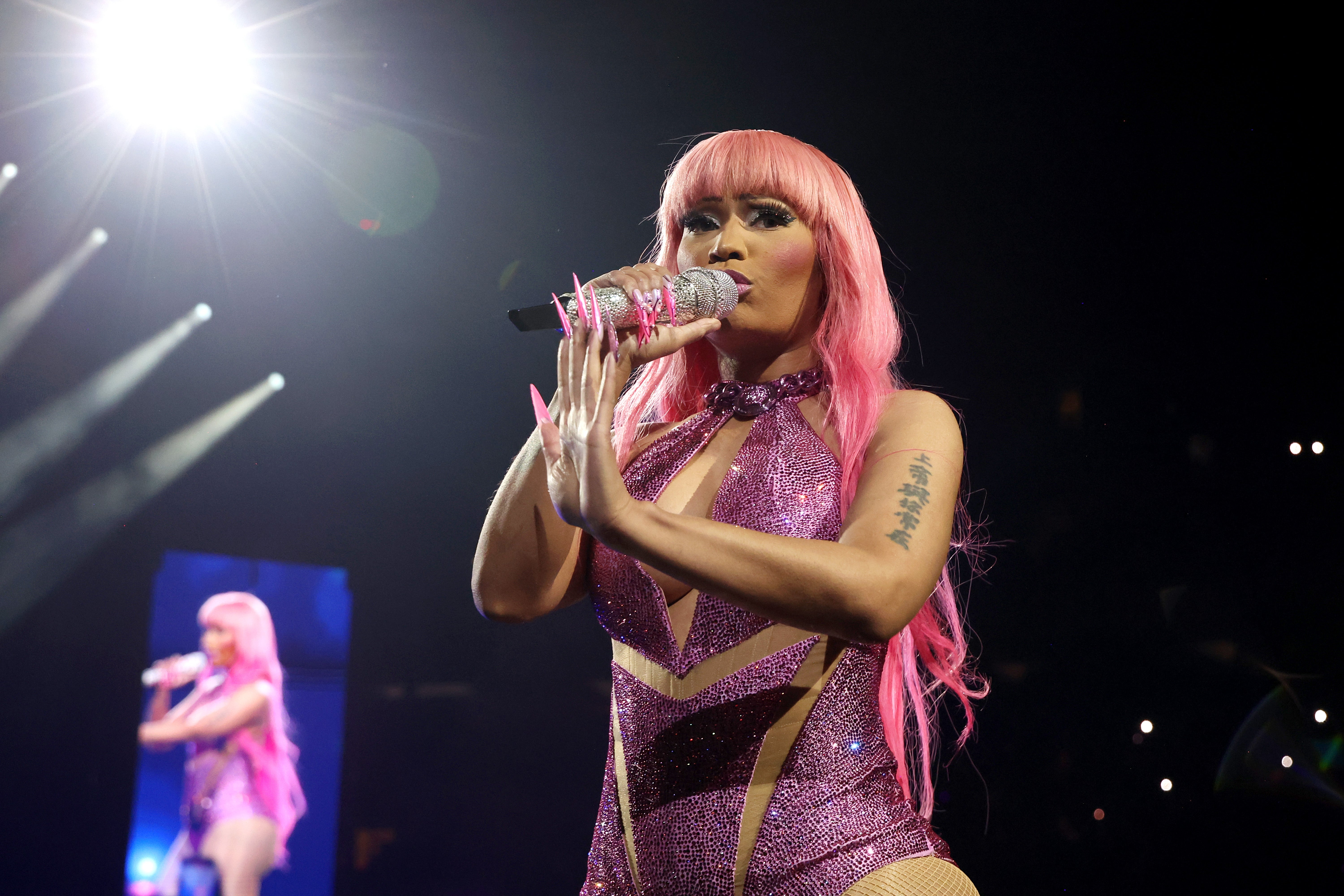 Nicki Minaj with agelong hairsbreadth and a sparkling outfit performs connected stage, holding a glittery microphone, nether agleam spotlight